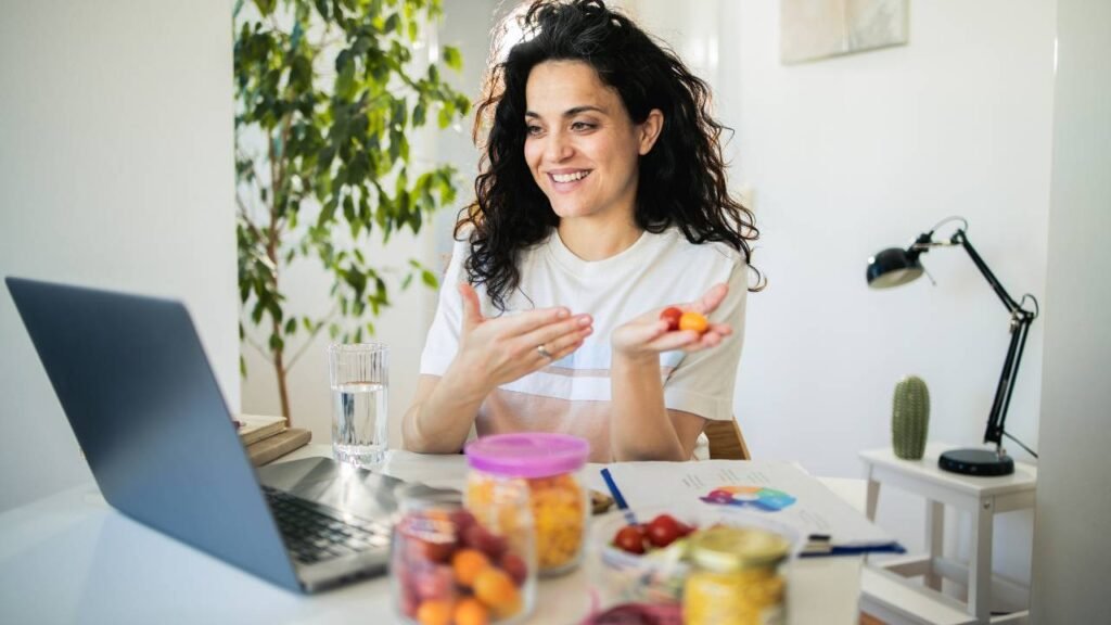 A woman smiling during an online diet consultation on her laptop, with fruit on the table